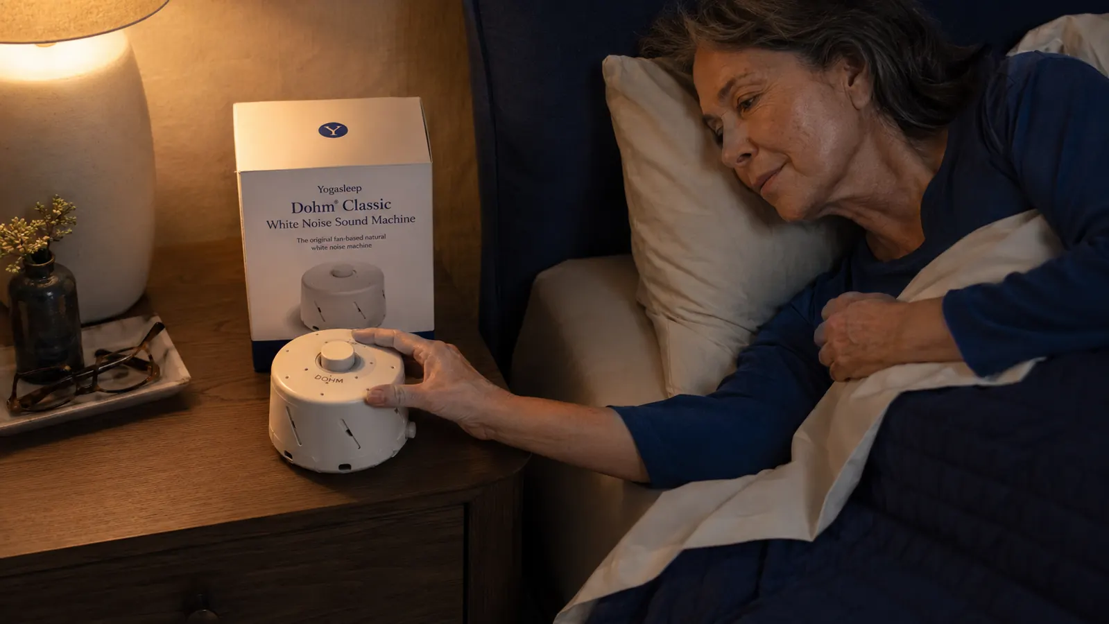 Close-up of the Yogasleep Dohm Classic white noise machine sitting on a nightstand next to a glass of water