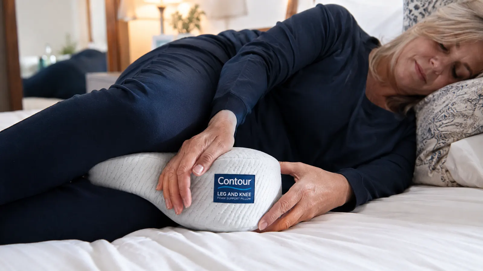 Close-up of a Contour Legacy knee pillow positioned between two knees on a white sheet