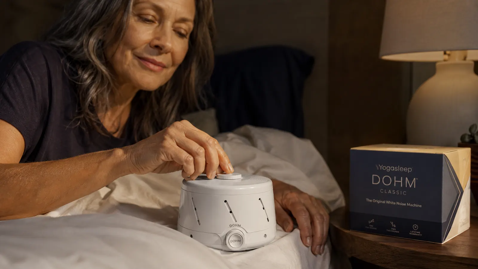 Hand adjusting the tone cap on the top of the Yogasleep Dohm Classic to fine-tune the white noise volume