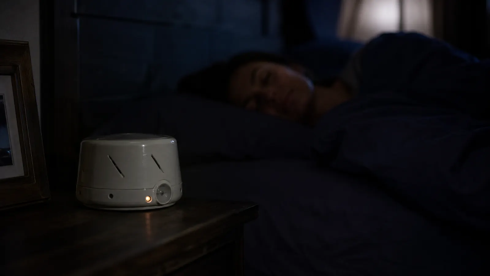 Cozy bedroom at night with the Dohm Classic glowing faintly on the nightstand, creating a sense of peaceful quiet