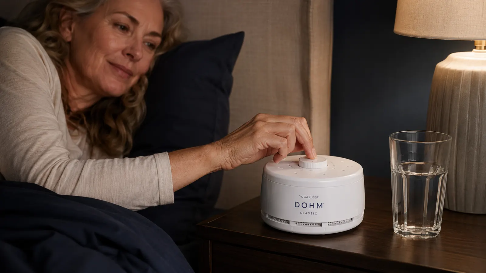 Yogasleep Dohm Classic white noise machine on a nightstand next to a glass of water